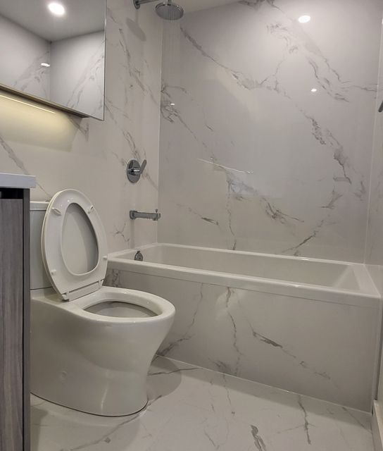 Modern bathroom renovation with marble-look tile, white toilet and bathtub